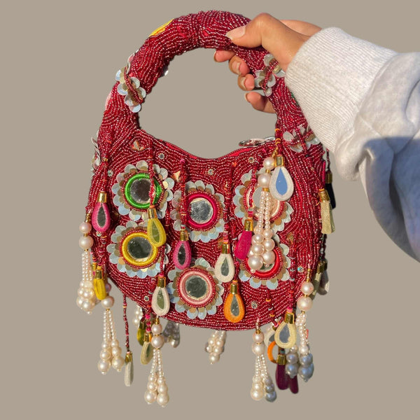 Vibrant red embroidered handbag with mirror work and pearl tassels, perfect for Indian weddings and festive occasions. This structured ethnic clutch features a sturdy handle and detailed thread work, making it an ideal accessory for bridal and party outfits. Pairs beautifully with lehengas, sarees, and anarkalis for a bold, traditional look with modern elegance.