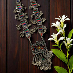 Aradhya German Silver Multicolor Ghungroo Necklace featuring intricate oxidized silver work with red, green, and blue enamel detailing. This handcrafted tribal statement necklace includes dangling ghungroos for a traditional boho look. Perfect ethnic jewelry piece for festivals, weddings, or cultural events. A stunning handmade long Afghan-style necklace that adds vintage and artistic charm to any outfit.