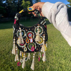 Black beaded bag with intricate mirror work, multicolor thread embroidery, and pearl tassels | Handmade Indian bridal clutch for weddings and festive occasions | Traditional ethnic handbag with beaded handle | Perfect accessory for sarees, lehengas, and anarkalis | Designer Indian party purse for brides and bridesmaids | Elegant and functional festive bag for cultural events and gifting.