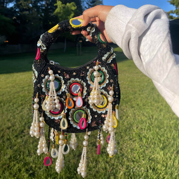 Black beaded bag with intricate mirror work, multicolor thread embroidery, and pearl tassels | Handmade Indian bridal clutch for weddings and festive occasions | Traditional ethnic handbag with beaded handle | Perfect accessory for sarees, lehengas, and anarkalis | Designer Indian party purse for brides and bridesmaids | Elegant and functional festive bag for cultural events and gifting.