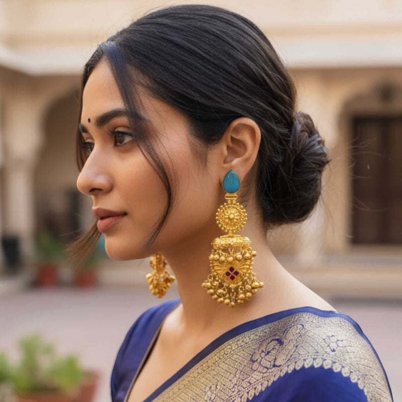 Woman wearing gold and turquoise earrings with a blurred background

. Model wearing handcrafted 92.5 silver gold-plated temple earrings adorned with ruby stones and ghungroos. The antique gold finish gives a regal touch, enhancing the traditional South Indian design. Perfect for weddings, festive occasions, or cultural celebrations, these earrings pair beautifully with sarees and lehengas. The intricate detailing and jingling ghungroos add timeless elegance to any ethnic or bridal look.