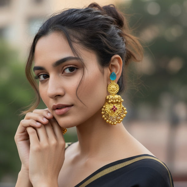 Woman wearing large, ornate gold earrings with a blurred background. Model wearing antique gold 92.5 silver temple earrings featuring intricate floral motifs, ruby stones, and traditional ghungroos (bells). The earrings have a rich antique gold plating and detailed craftsmanship, adding elegance and cultural charm. Perfect for South Indian bridal looks, festive celebrations, or traditional events. These handcrafted earrings beautifully complement sarees, lehengas, and ethnic outfits for an elegant statement