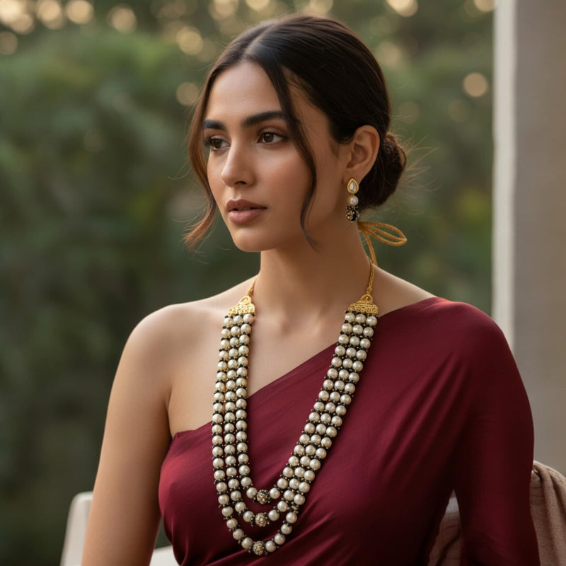 Model showcasing the Fatiha Long Pearl Necklace with Earrings, a multi-layer Indian pearl mala featuring ivory pearls, black beads, Kundan accents, and Meenakari gold-plated detailing. Styled with a maroon saree, the long pearl necklace and matching Kundan earrings highlight traditional Indian bridal jewelry perfect for weddings, festivals, and ethnic fashion.