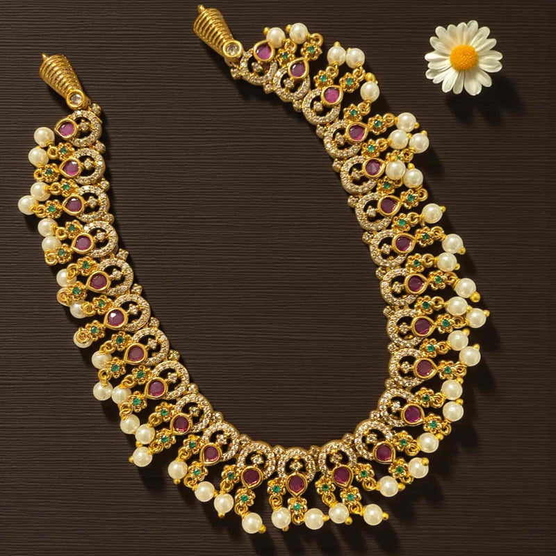 Gold necklace set with matching earrings featuring CZ, ruby, and emerald stones in an intricate gold-plated design. The necklace has pearl drops that add elegance and movement, while the earrings complement the look perfectly. Displayed on a wooden background with a white rose, this South Indian jewelry set reflects traditional craftsmanship, ideal for brides, weddings, and festive occasions.