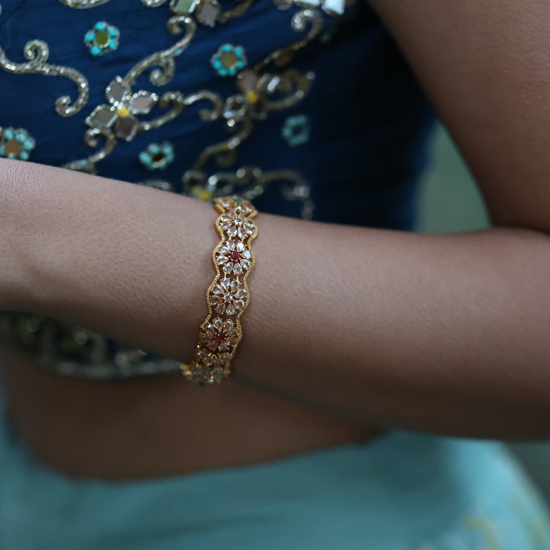 Indian Online Jewelry featuring model wearing gold plated bangle with polki, emerald and ruby stones.