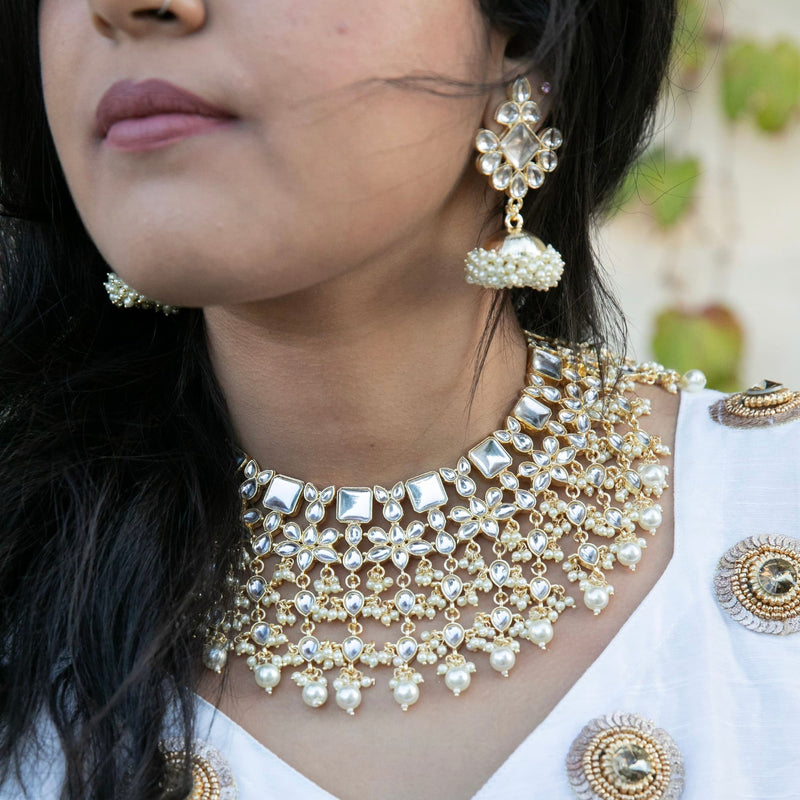 Model wearing a four layer kundan necklace with jhumkas make with kundan and pearls on gold plating.