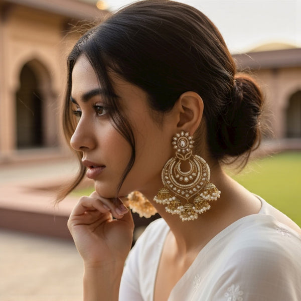 Model wearing high quality Kundan and pearl gold plated chandbali earrings showcasing elegant Indian craftsmanship. The earrings feature intricate Kundan detailing with delicate pearl drops that highlight the model’s festive look. Perfect for weddings, receptions, or parties, these Polki-inspired earrings add a regal touch to any outfit. The gold plating and pearl accents shine beautifully, making them ideal for modern women who love timeless Indian jewelry with luxurious charm.
