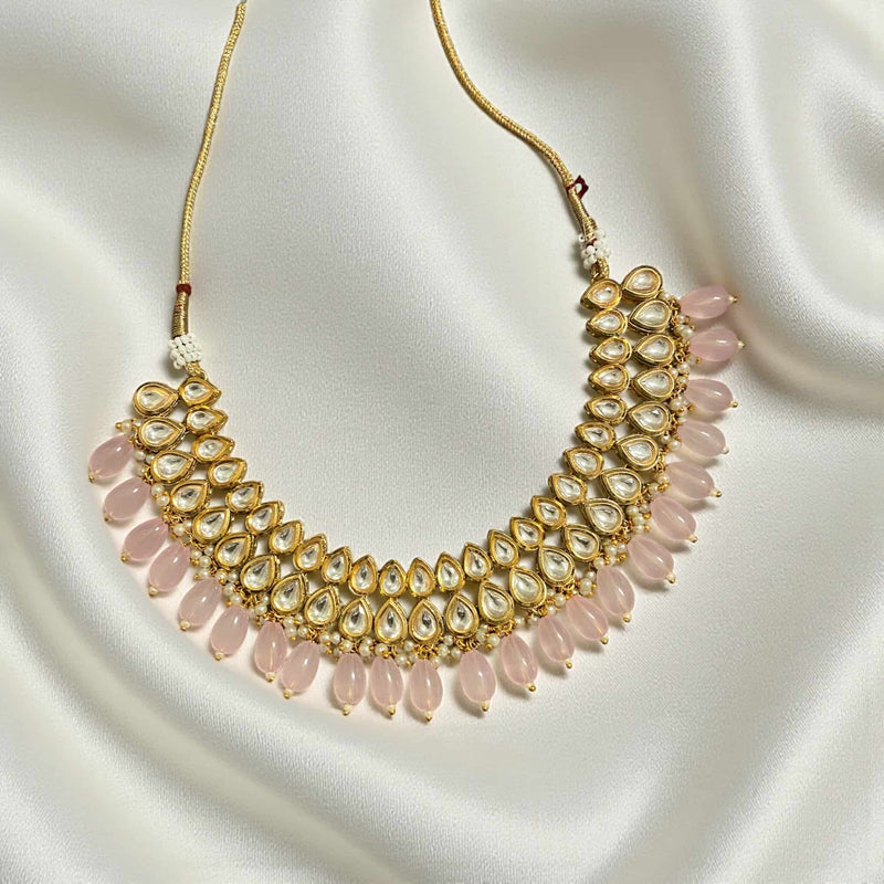 Gold plated Kundan necklace with soft pink beads displayed on a green background. Handcrafted traditional Indian jewelry perfect for weddings, receptions, and festive outfits. Elegant statement necklace designed to pair with sarees, lehengas, and anarkalis.