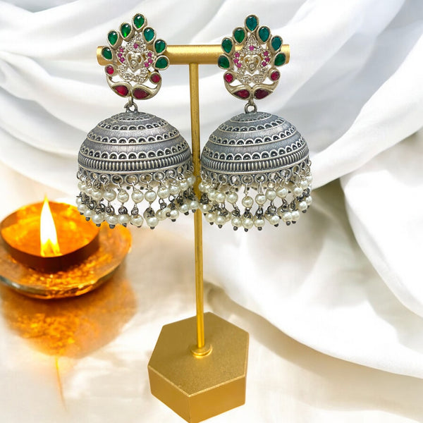Nishali Oxidized Jhumka Earrings with intricate dome detailing, pearl drops, and a peacock-inspired stud adorned with emerald green and ruby red stones. These handcrafted earrings feature high-quality oxidized silver work and traditional South Asian design, perfect for festive occasions, weddings, and ethnic wear. A striking piece of Indian jewelry and Pakistani jewelry that combines elegance, cultural richness, and timeless craftsmanship.