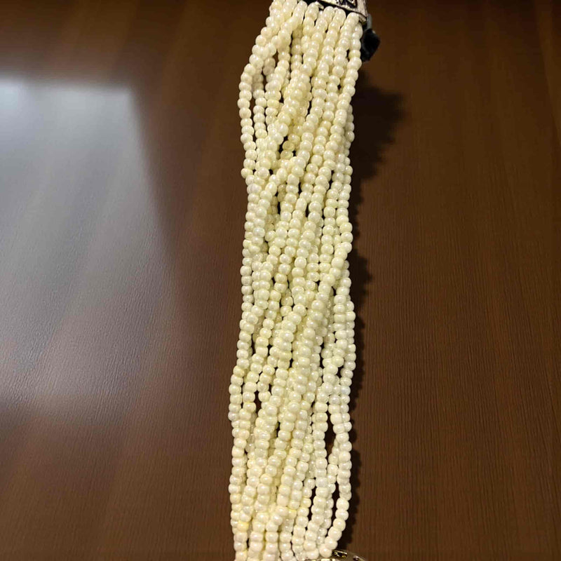 String of rice pearl on a wooden surface. Handcrafted Kundan pearl necklace set in a gold and silver finish with shimmering CZ detailing. The centerpiece pendant features silver foil Polki stones surrounded by a halo of brilliance. Accompanied by matching statement earrings, this necklace is designed for weddings, festive occasions, and celebrations, bringing a graceful, regal look to any traditional Indian outfit.