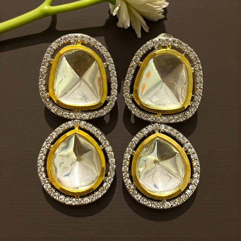 Two gold and silver teardrop-shaped gemstone earrings on a dark surface with a white flower in the background.Elegant Kundan earrings featuring large silver foil Polki stones bordered with sparkling Cubic Zirconia. Each earring has a teardrop design framed in gold and silver tones, reflecting exquisite craftsmanship and regal charm. Perfect for weddings, festive occasions, or parties, these statement earrings pair beautifully with traditional sarees and lehengas, adding a royal glow to your ethnic look.