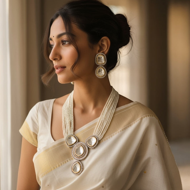 Woman wearing a traditional outfit with jewelry indoors. Elegant model showcasing a stunning pearl necklace featuring lustrous pearls and intricate silver foil Kundan work. The necklace sits gracefully around her neck, reflecting light beautifully. Perfect for weddings, festive occasions, or traditional celebrations, highlighting fine craftsmanship and premium quality. Close-up view emphasizes the delicate design, sparkling stones, and luxurious finish, making it ideal for bridal or ethnic jewelry collectio