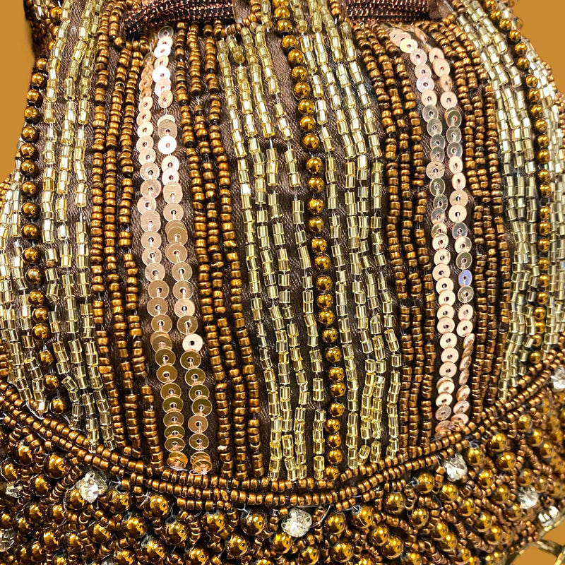 Close-up of a beaded and sequined fabric with gold and brown tones. Luxury golden sequin potli bag for women featuring detailed beadwork, shimmering sequins, and elegant tassel accents. Perfect Indian bridal clutch for weddings, sangeet, and festive occasions. Handmade ethnic handbag with drawstring closure and beaded handle for a regal finish. Traditional gold potli purse ideal for pairing with lehengas, sarees, and party outfits.Designer festive potli pouch for brides, bridesmaids,and special celebration.