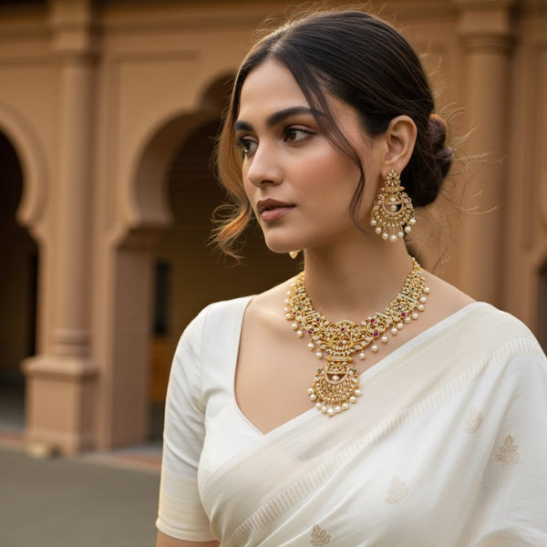 Woman wearing a gold CZ necklace set with sparkling cubic zirconia, ruby stones, emerald accents, and pearl drops. Traditional Indian bridal jewelry styled with elegant attire. Close-up showing intricate gold plating and premium craftsmanship. Perfect for weddings, receptions, festivals, and special occasions. High-quality South Asian necklace set ideal for brides and party outfits.