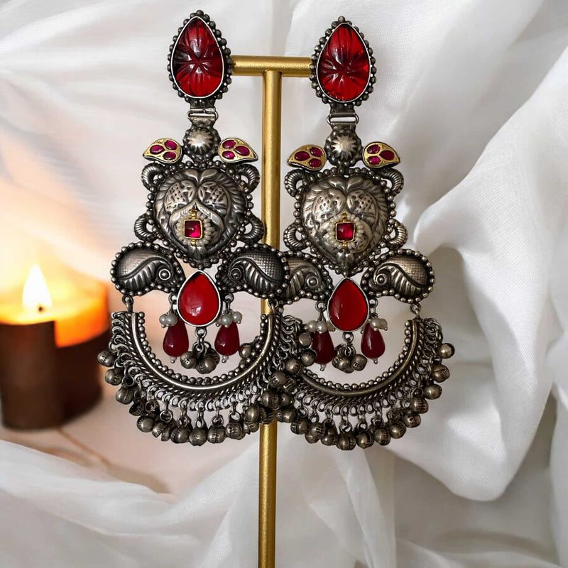 Bold oxidized silver chandbali earrings with intricate design and vibrant ruby carved stones, perfect for boho-chic fashion lovers. The antique finish, paired with traditional ghungroos and deep red accents, creates a statement piece that complements fusion, Indo-western, and festival wear. A must-have for fashion-forward individuals seeking a unique blend of heritage and edgy style. Lightweight and eye-catching for concerts, cultural events, or everyday flair.