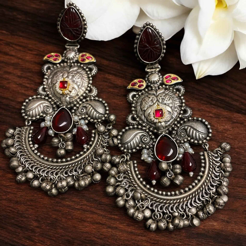 Oxidized silver long earrings with intricate design, featuring a ruby red Kundan stone at the center, detailed carvings, ghungroos, and teardrop-shaped carved stones. The earrings showcase traditional Indian craftsmanship with tribal and ethnic charm, perfect for festive occasions, weddings, or boho styling. The antique silver finish and hanging elements add movement and elegance, making them a standout accessory in any South Asian or fusion ensemble.
