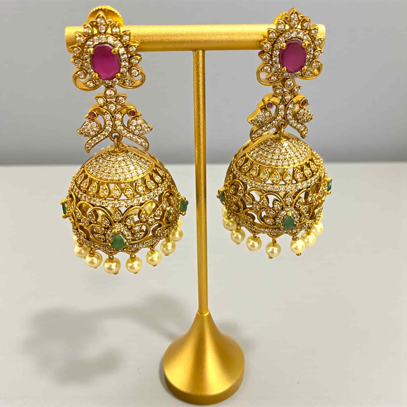 Gold-plated jhumka earrings with cubic zirconia, ruby, and emerald stones plus pearl hangings. Traditional Indian jewelry with beautiful craftsmanship. Perfect statement earrings for saree, gown, or festive attire.