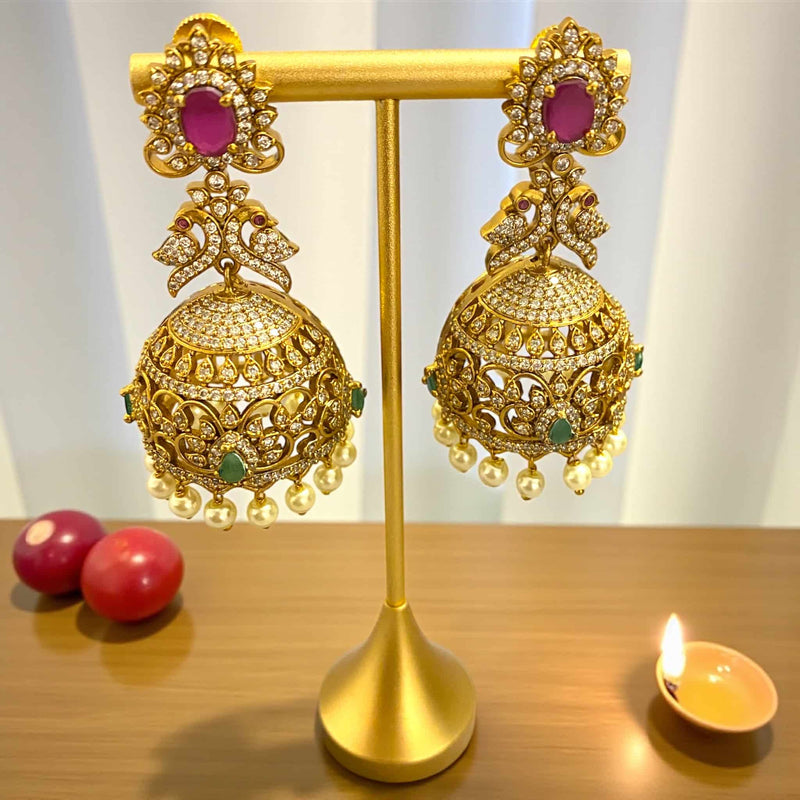 Traditional gold-plated cubic zirconia jhumka earrings featuring ruby and emerald stones with intricate dome design and pearl drops. Ideal for bridal wear, festive looks, and ethnic fashion styles. Elegant jewelry piece for special occasions.