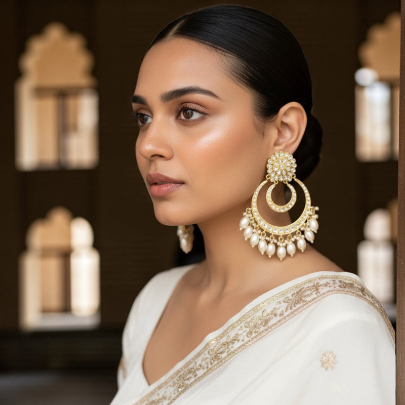 Model wearing gold plated Kundan chandbali earrings with pearl drops, styled with a traditional Indian outfit. The handcrafted earrings feature intricate Kundan stonework and a circular gold design with delicate pearls that enhance their elegance. Perfect for weddings, festivals, and special occasions, these statement earrings highlight the beauty of Indian craftsmanship and timeless ethnic style.