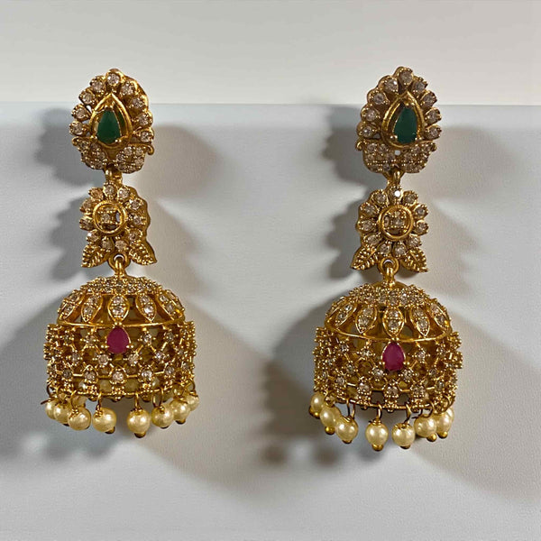 Ornate gold earrings with gemstones on a white background. Gold-plated jhumka earrings featuring intricate CZ detailing with ruby and emerald stones. Traditional Indian bridal earrings with dome-shaped design and delicate pearl drops. Elegant ethnic jewelry perfect for weddings, parties, and festive occasions. South Asian gold jhumka earrings with sparkling stones and handcrafted detailing.