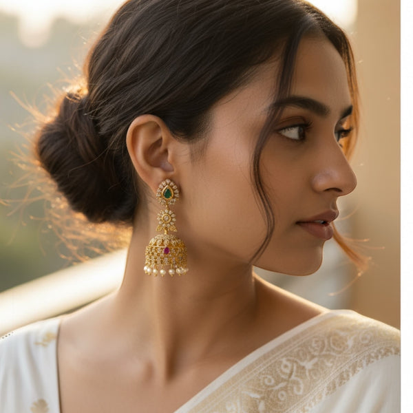 Woman wearing gold earrings with a blurred natural background.  Model wearing stunning traditional gold jhumka earrings adorned with sparkling cubic zirconia, vibrant ruby and emerald stones. These intricate Indian earrings feature detailed craftsmanship and elegant design, perfect for weddings, festive occasions, or special celebrations. The earrings enhance the model’s ethnic outfit, highlighting South Asian jewelry style, and add a touch of luxury and glamour to any ensemble for bridal or party wear.