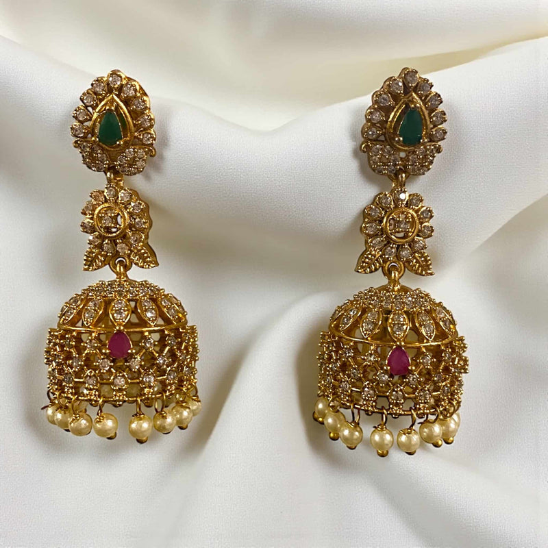 Ornate gold earrings with gemstones on a white fabric background. Gold jhumka earrings adorned with sparkling cubic zirconia, ruby, and emerald stones, featuring intricate traditional Indian craftsmanship. These elegant earrings showcase detailed filigree work, perfect for weddings, festive occasions, and special celebrations. The jhumkas highlight classic South Asian jewelry design, combining vibrant gemstones with gold finish, making them a statement accessory for bridal or ethnic wear, adding charm.