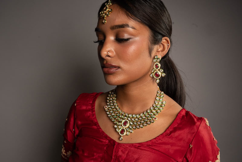 Girl wearing a Reverse American Diamond/Cubic Zirconia Necklace Set which has ruby stones. The set has a heavy neckace, earrings and maag tikka.